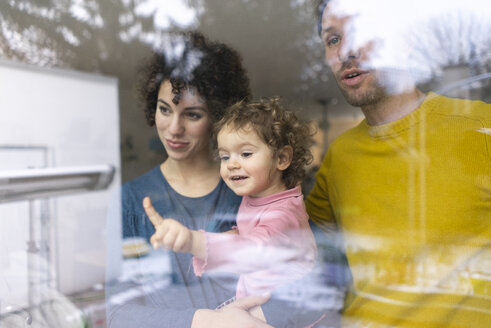 Familie schaut aus dem Fenster, Mutter trägt Tochter, zeigt auf sie - JOSF03103
