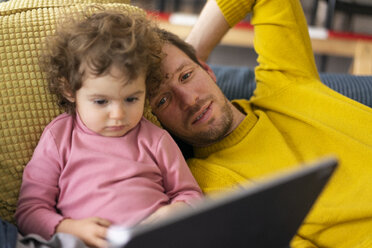 Father and daughter lying on couch watching movie on theit tablet - JOSF03112