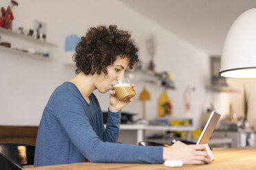 Junge Frau sitzt am Tisch, benutzt ein digitales Tablet und trinkt Kaffee - JOSF03118