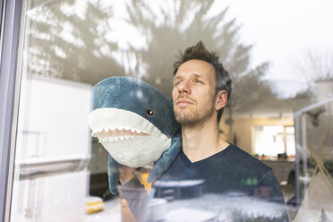 Mann schaut aus dem Fenster und trägt einen Spielzeug-Hai auf der Schulter - JOSF03121