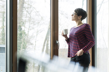 Woman with coffee mug looking out of terrace door - SBOF01824