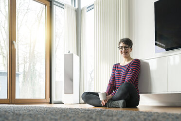 Portrait of laughing woman sitting on the floor of living room - SBOF01826