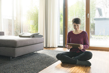 Porträt einer Frau, die auf dem Boden eines Wohnzimmers sitzt und ein digitales Tablet benutzt - SBOF01829