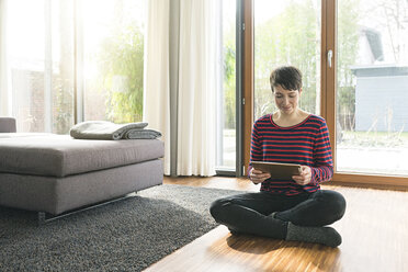 Portrait of woman sitting on the floor of living room using digital tablet - SBOF01829