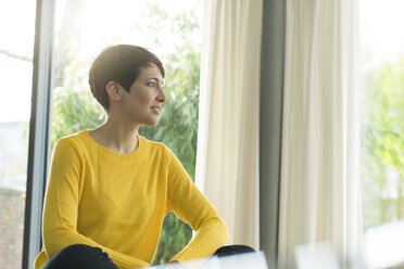 Woman sitting in the living room looking out of window - SBOF01835