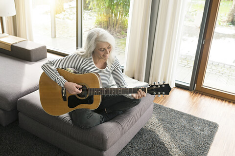 Mature woman sitting on couch at home playing guitar stock photo