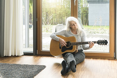 Reife Frau sitzt auf dem Boden des Wohnzimmers und spielt Gitarre - SBOF01840