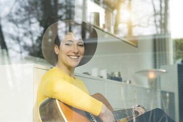 Porträt einer lächelnden Frau hinter einer Fensterscheibe, die Gitarre spielt - SBOF01843