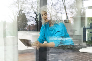 Porträt einer lächelnden reifen Frau, die zu Hause auf der Couch sitzt und auf ein digitales Tablet schaut - SBOF01854