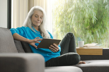 Portrait of mature woman sitting on the couch at home using digital tablet - SBOF01857