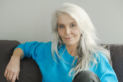 Portrait of smiling mature woman sitting on the couch at home stock photo