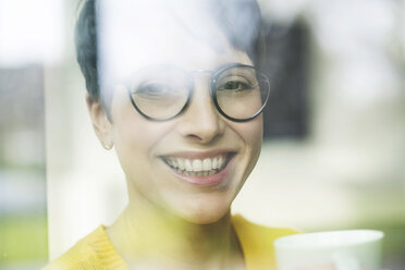 Porträt einer lachenden Frau mit einer Tasse Kaffee hinter einer Fensterscheibe - SBOF01865