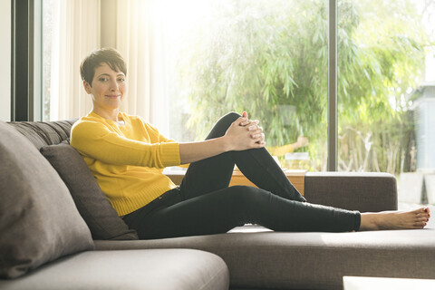 Porträt einer lächelnden Frau, die sich zu Hause auf der Couch entspannt, lizenzfreies Stockfoto