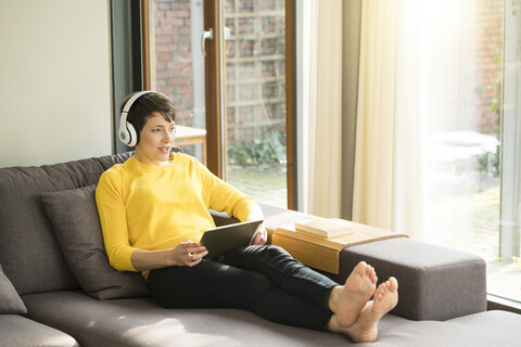 Portrait of woman with digital tablet sitting on the couch at home listening music with headphones stock photo