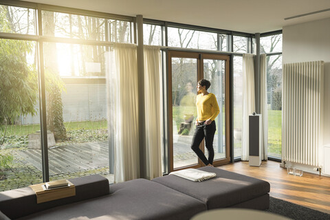 Woman standing in living room in the evening looking through terrace door stock photo