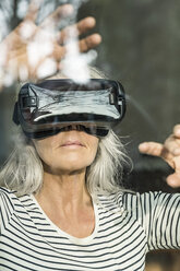 Portrait of mature woman behind windowpane using Virtual Reality Glasses - SBOF01883