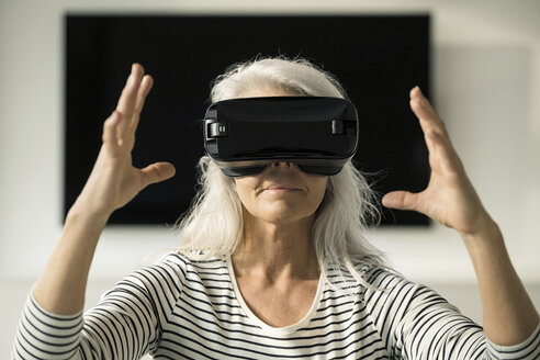 Porträt einer reifen Frau, die eine Virtual-Reality-Brille zu Hause benutzt - SBOF01885