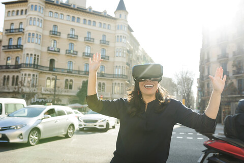 Aufgeregte Frau mit VR-Brille in der Stadt, lizenzfreies Stockfoto