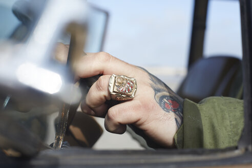 Man's hand with ring and tattoo at car steering wheel - AMEF00028