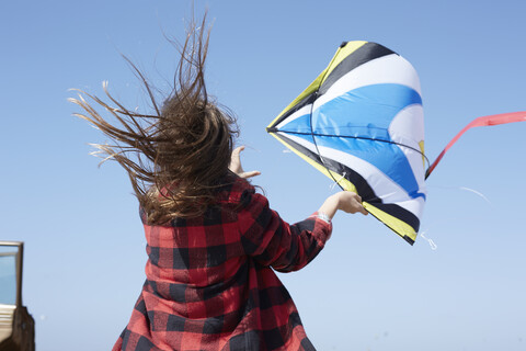 Mädchen mit zerzaustem Haar lässt Drachen unter blauem Himmel steigen, lizenzfreies Stockfoto