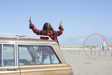 Germany, St Peter-Ording, girl flying kite on the beach from a car stock photo