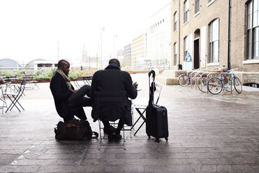 Two travelling businessmen sitting at pavement cafe working - IGGF00923