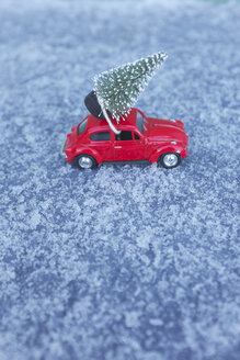 Rotes VW-Käfer-Spielzeugauto mit Weihnachtsbaum auf dem Dach in verschneiter Umgebung - GISF00400