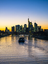 Germany, Hesse, Frankfurt, Skyline of financial district, Main river and Deutschherrn Bridge, cargo ship at sunset - AMF06812