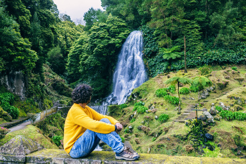 Portugal, Azoren-Inseln, Sao Miguel, sitzender Mann mit Blick auf einen Wasserfall, lizenzfreies Stockfoto