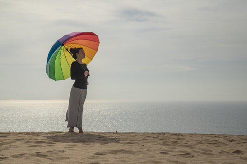 Frau mit buntem Regenschirm am Strand stehend - KBF00550