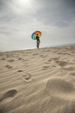 Frau mit buntem Regenschirm am Strand stehend, lizenzfreies Stockfoto