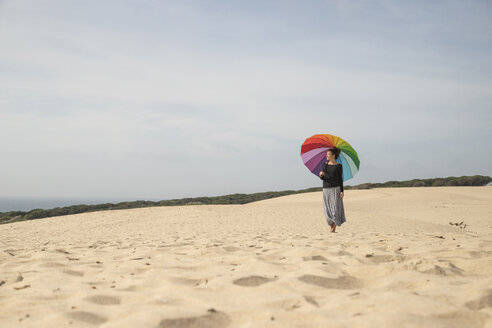 Frau mit buntem Regenschirm steht auf einer Düne und schaut in die Ferne - KBF00555