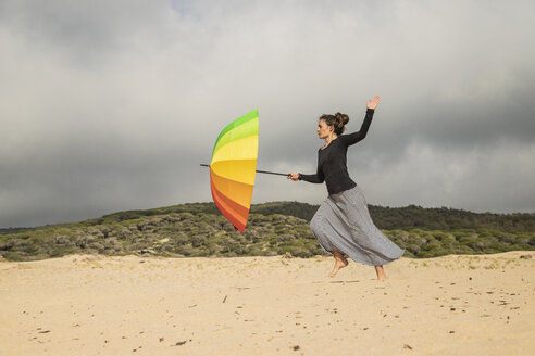 Frau hält bunten Regenschirm auf einer Düne - KBF00556