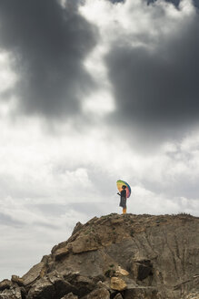 Woman with colorful umbrella standing on a hill at the beach - KBF00557