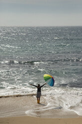 Frau mit buntem Regenschirm am Strand stehend, mit erhobenen Armen - KBF00562