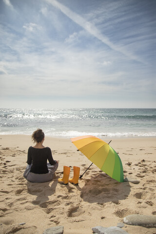 Woman with colorful umbrella sitting on the beach, rear view stock photo