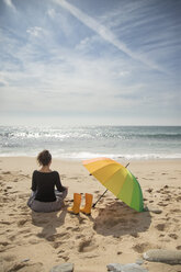 Frau mit buntem Regenschirm am Strand sitzend, Rückansicht - KBF00563