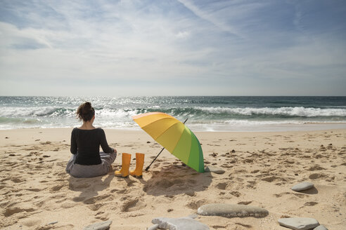 Frau mit buntem Regenschirm am Strand sitzend, Rückansicht - KBF00564