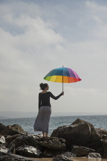 Frau hält bunten Regenschirm am felsigen Strand, Rückansicht - KBF00565