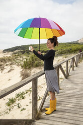 Frau mit buntem Regenschirm steht am Strand und macht ein Selfie - KBF00568