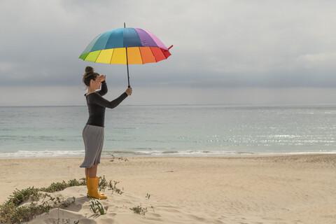 Frau mit buntem Regenschirm sitzt am Strand, lizenzfreies Stockfoto