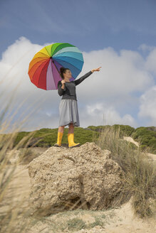 Frau mit buntem Regenschirm steht auf einem Felsen und schaut in die Ferne - KBF00572