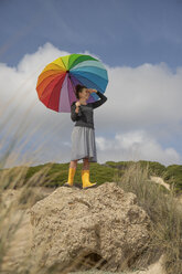 Frau mit buntem Regenschirm steht auf einem Felsen und schaut in die Ferne - KBF00573