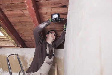 Dachisolierung, Arbeiter bohrt Holzplatte mit einem Akkubohrer - SEBF00025