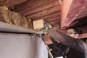 Dachisolierung, Arbeiter, der ein Steildach mit Holzfaserdämmung ausfüllt - SEBF00029