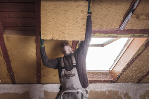 Dachisolierung, Arbeiter, der ein Steildach mit Holzfaserdämmung ausfüllt - SEBF00037