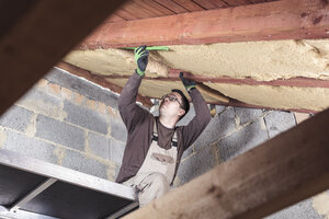 Dachisolierung, Arbeiter, der ein Steildach mit Holzfaserdämmung ausfüllt - SEBF00041