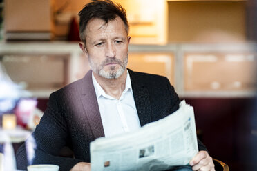 Portrait of mature businessman sitting in a coffee shop reading newspaper - DIGF06003