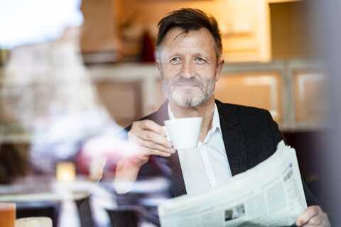 Portrait of smiling mature businessman with newspaper in a coffee shop drinking coffee stock photo