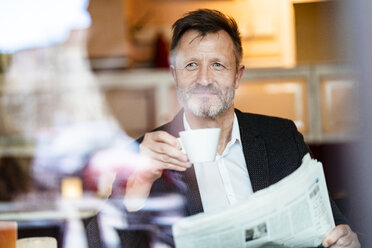 Portrait of smiling mature businessman with newspaper in a coffee shop drinking coffee - DIGF06004